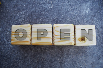 Open - wooden blocks letters on grey background.