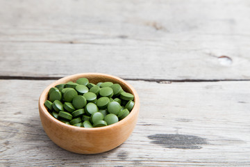 green pills spirulina or chlorella seaweed in the wooden bowl. green barley chlorella