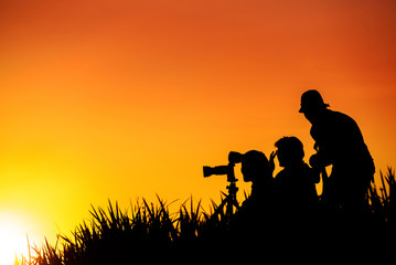 Silhouette of photographers group on grass hill in sunset evening
