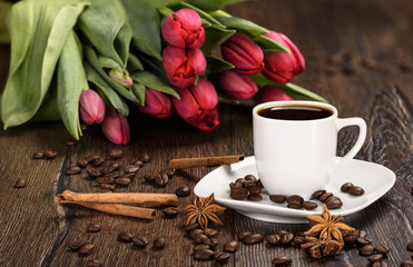 Black coffee in a white cup on a background of red tulips