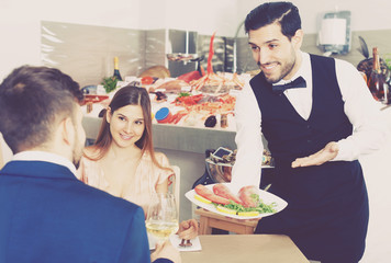 waiter serving tasty fish carpaccio to young couple