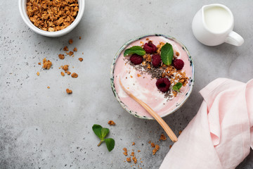 Pink raspberry banana smoothie bowl with granola, chia seeds, coconut and mint on light gray concrete background. Selective focus. Top view. Copy space.