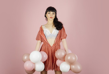 Sexy woman in white bra holds balloons on pink background.