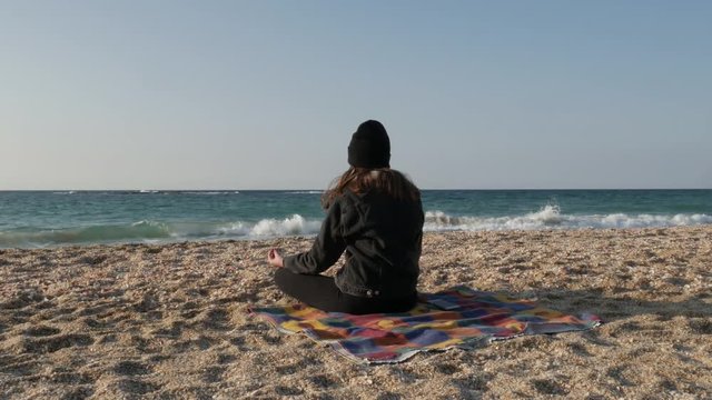 Girl in warm clothes meditates on the shore of the Mediterranean Sea on a cool autumn day.