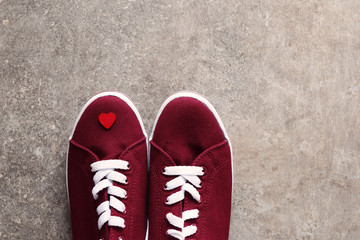 Two red new sneakers with white laces and little red heart on one of it on grey brown grunge background. Horizontal top view.