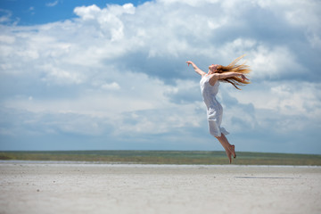 Obraz premium A woman in a white dress jumps high against a background of a sky landscape with a desert. 