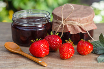 Traditional homemade strawberry jam in jars with fresh strawberries on wooden desk