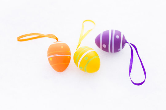 Closeup of purple, orange and yellow easter eggs with ribbons and decorated with stripes and dots laying outdoors on fresh snow in spring