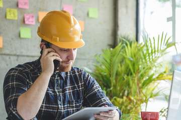 Engineer talking with phone and looking at tablet in office.