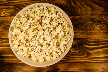 Ceramic plate with popcorn on wooden table. Top view
