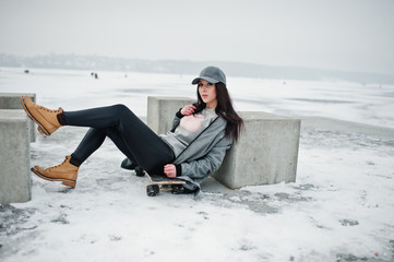 Fototapeta na wymiar Stylish brunette girl in gray cap, casual street style with skate board on winter day.