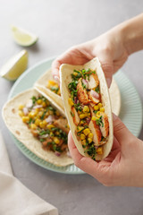 Hands holding tacos with roasted chicken meat, corn, parsley, salsa and sweet pepper.