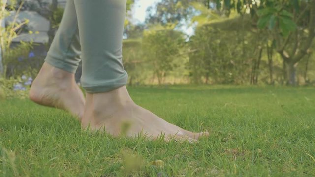 Close-up feet of barefoot girl at domestic garden with green lawn in slow motion