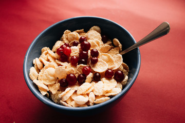 Delicious crispy cornflakes with kiwi pieces and cranberries in bowl, healthy breakfast on red backgroun