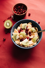 delicious crispy cornflakes with kiwi pieces and cranberries in bowl,  healthy breakfast on red background