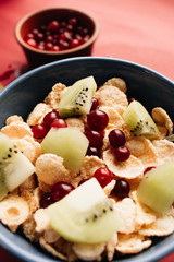 delicious crispy cornflakes with kiwi pieces and cranberries in bowl,  healthy breakfast on red background
