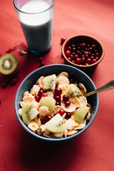 delicious crispy cornflakes with kiwi pieces and cranberries in bowl,  healthy breakfast on red background