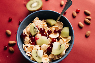 Delicious crispy cornflakes with kiwi pieces and cranberries in bowl, healthy breakfast on red backgroun