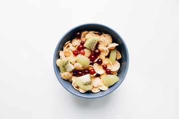 delicious crispy cornflakes with kiwi pieces and cranberries in bowl on white background, closeup, healthy breakfast 