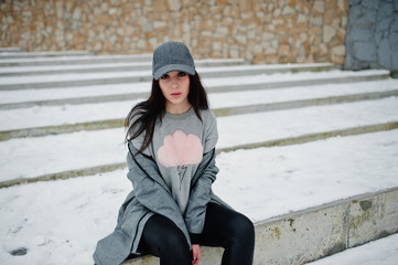 Fototapeta premium Stylish brunette girl in gray cap, casual street style on winter day against colored wall.