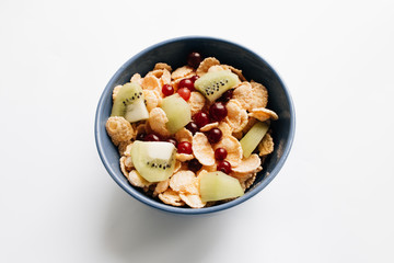 delicious crispy cornflakes with kiwi pieces and cranberries in bowl on white background, closeup, healthy breakfast 