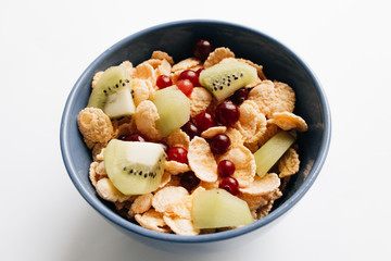 delicious crispy cornflakes with kiwi pieces and cranberries in bowl on white background, closeup, healthy breakfast 