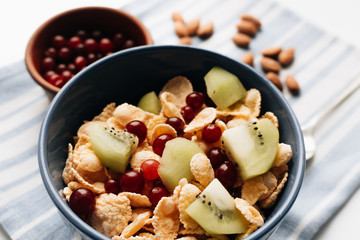 delicious crispy cornflakes with kiwi pieces and cranberries in bowl, almonds on dish cloth, closeup, healthy breakfast 