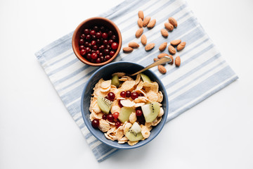 glass of milk, delicious crispy cornflakes with kiwi pieces and cranberries in bowl, almonds on dish cloth, closeup, healthy breakfast 