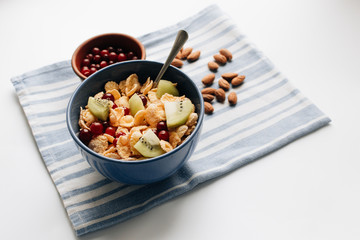 glass of milk, delicious crispy cornflakes with kiwi pieces and cranberries in bowl, almonds on dish cloth, closeup, healthy breakfast 