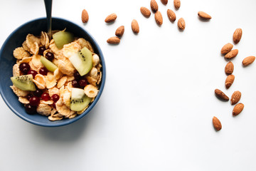 delicious crispy cornflakes with kiwi pieces and cranberries in bowl, almonds scattered on white background, closeup, healthy breakfast 