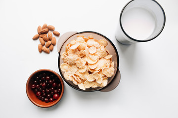 delicious crispy cornflakes in bowl with cranberries, glass of milk and almonds  on white background,  healthy breakfast