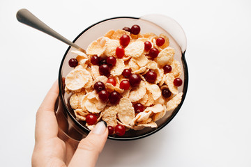 female hand holding bowl with delicious crispy cornflakes and cranberries on white background, closeup, healthy breakfast 