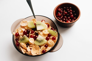 delicious crispy cornflakes with kiwi pieces and cranberries in bowl on white background, closeup, healthy breakfast 