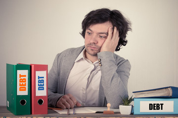 Debt text on the binders, worried bussinesman thinking by the work desk.