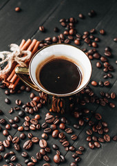 Cup of black coffee, coffee beans and cinnamon sticks on dark background