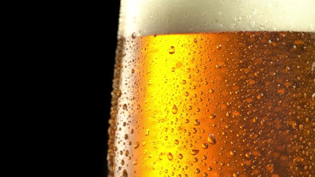 Glass of beer turns slowly around its axis. Close up 4K video. Black background.