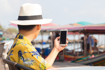 Fototapeta premium View from inside of young man wearing vintage style shirt with brim hat and using smartphone for communication at harbor. Travel in Chantaburi Province, Thailand. Soft focus and blur. Tourist concept.