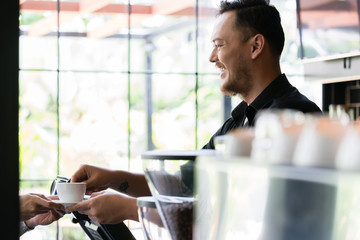 Side view of a young friendly bartender serving a short espresso to a customer in a modern coffee...