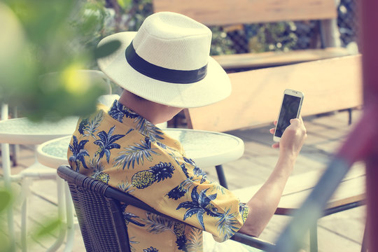 View From Back Of Young Man Wearing Vintage Style Shirt Using Smartphone To Take A Photo With Motorboat At Harbor. Travel In Chantaburi Province, Thailand. Soft Focus And Blur. Tourist Concept.