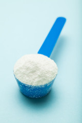 Plastic measuring spoon with milk powder, close-up.