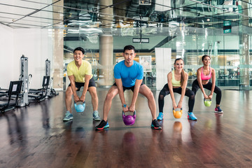 Full length view of four fit and cheerful young people smiling while holding heavy kettlebells...