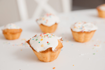 Close-up cupcakes decorated with white cream and colored caramel for the Easter holiday. In the background is white table.