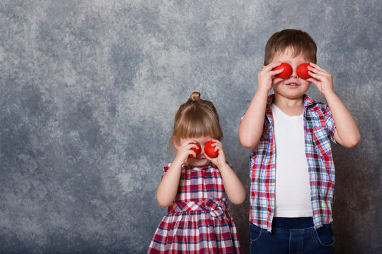 Two children, a girl and a boy dressed in checkered clothes. They hold red wooden Easter eggs in their hands.