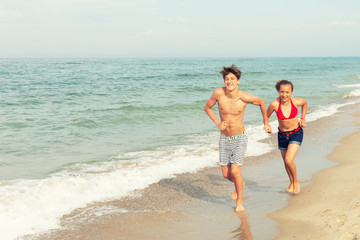 Two teenagers: a girl and a boy with blond hair, dressed in a swimsuit run, laugh and play in the sea beach.