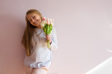 A young beautiful girl with blond long loose hair, keeps spring flowers in the hands of a sunny day. She smiling. Copy space.