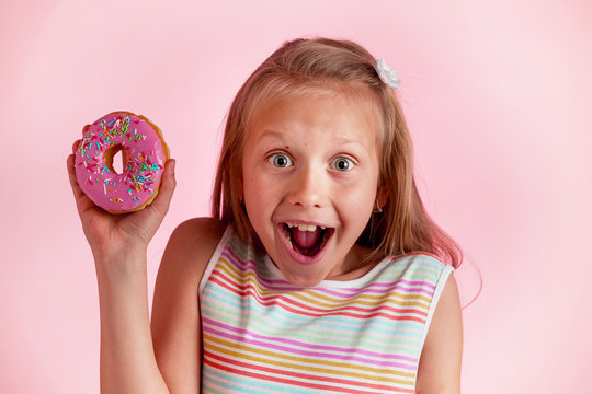 young beautiful happy and excited blond girl 8 or 9 years old holding donut on her hand looking spastic and cheerful in sugar addict concept