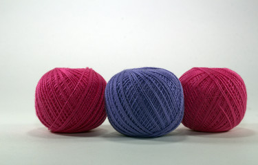 two burgundy and one lilac tangle of natural cotton thread for needlework on white background close-up