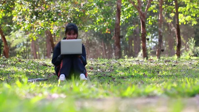 Education Learning Studying concept : Attractive Happy Asian Young girl enjoy  searching, social with laptop for preparing final test exam at green grass in public park on vacation time in summer day.