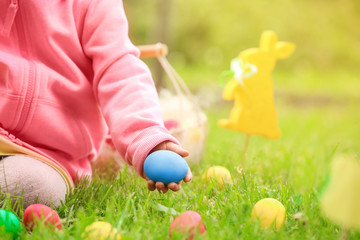 Little girl gathering colorful egg in park. Easter hunt concept