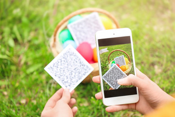 Woman scanning QR Code at park. Easter egg hunt concept